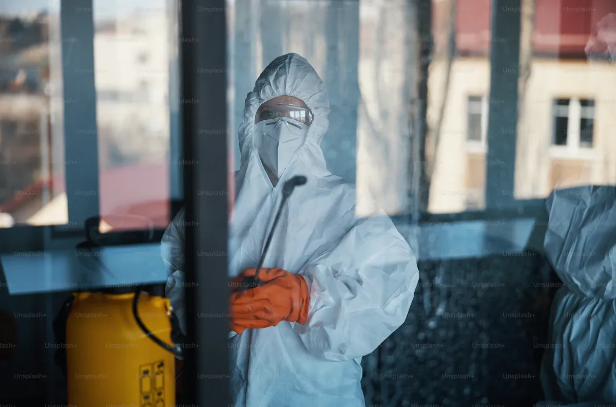Intervenant en combinaison intégrale pulvérisant un produit de décontamination